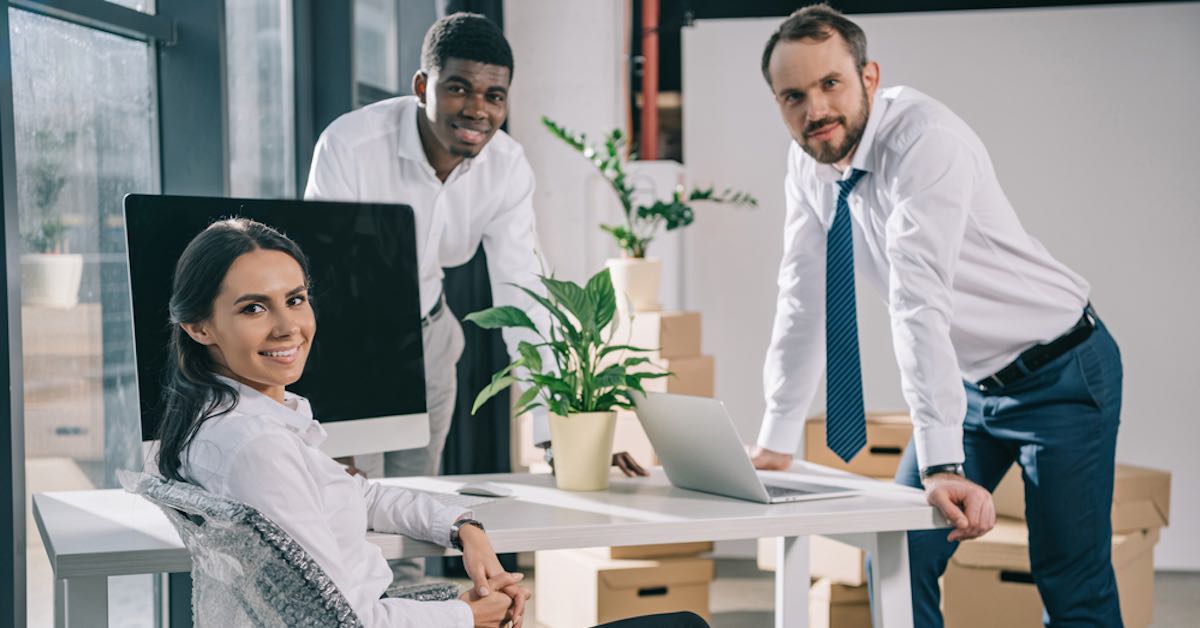 3 Employees at the office next to an office desk