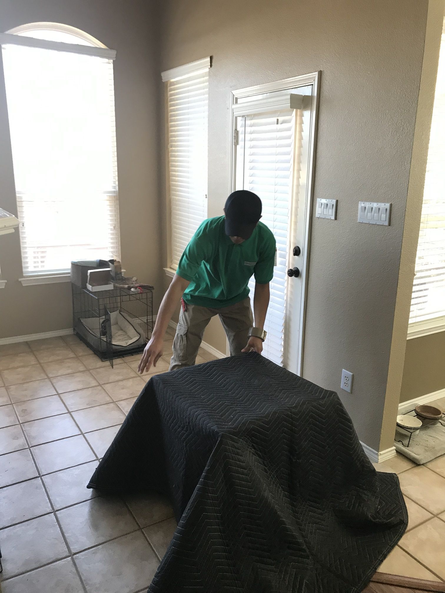 A Green Van Lines mover draping a quilted moving pad over furniture before it is carried out