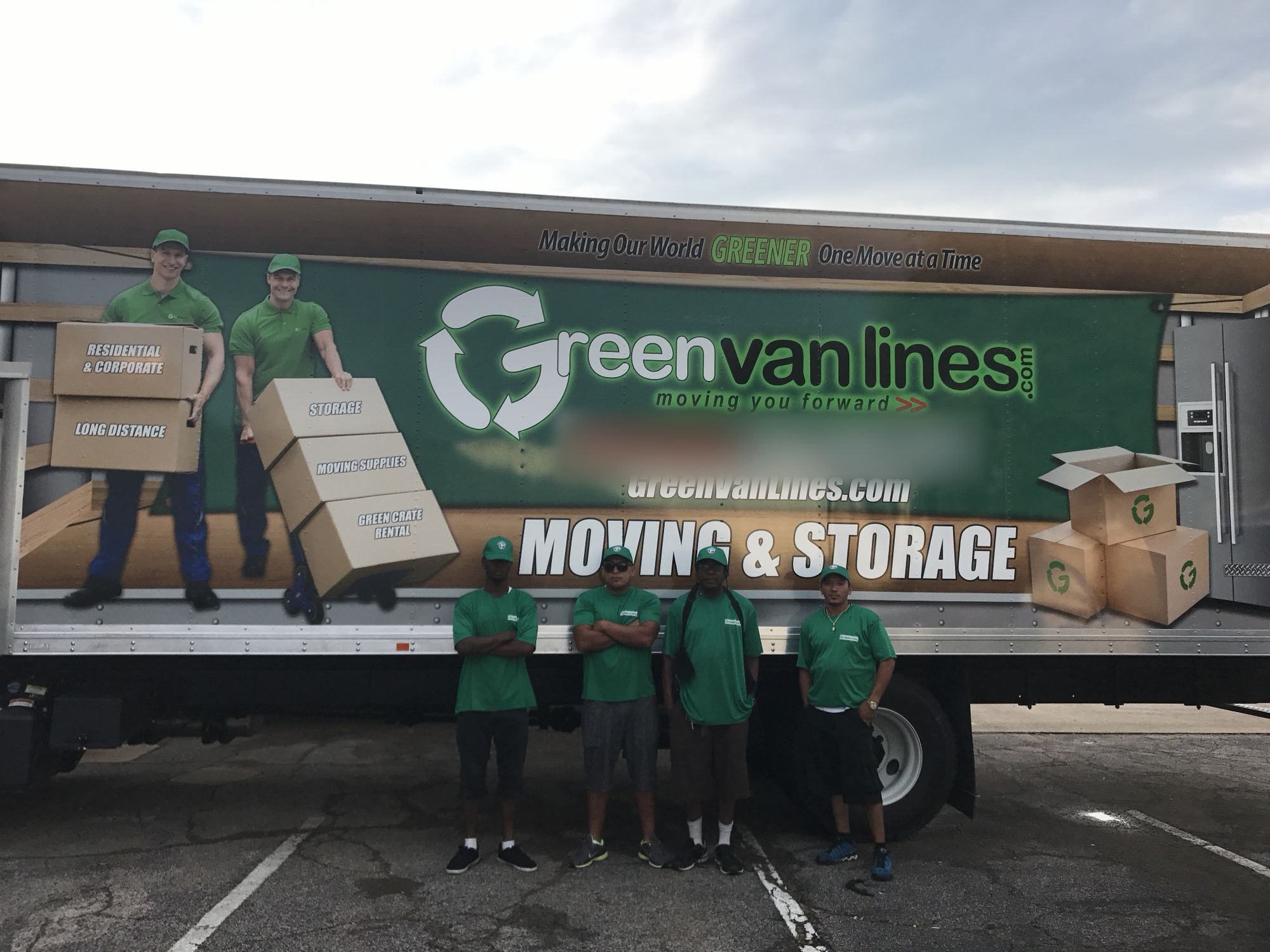 Four Green Van Lines movers in green uniforms standing in front of a company truck