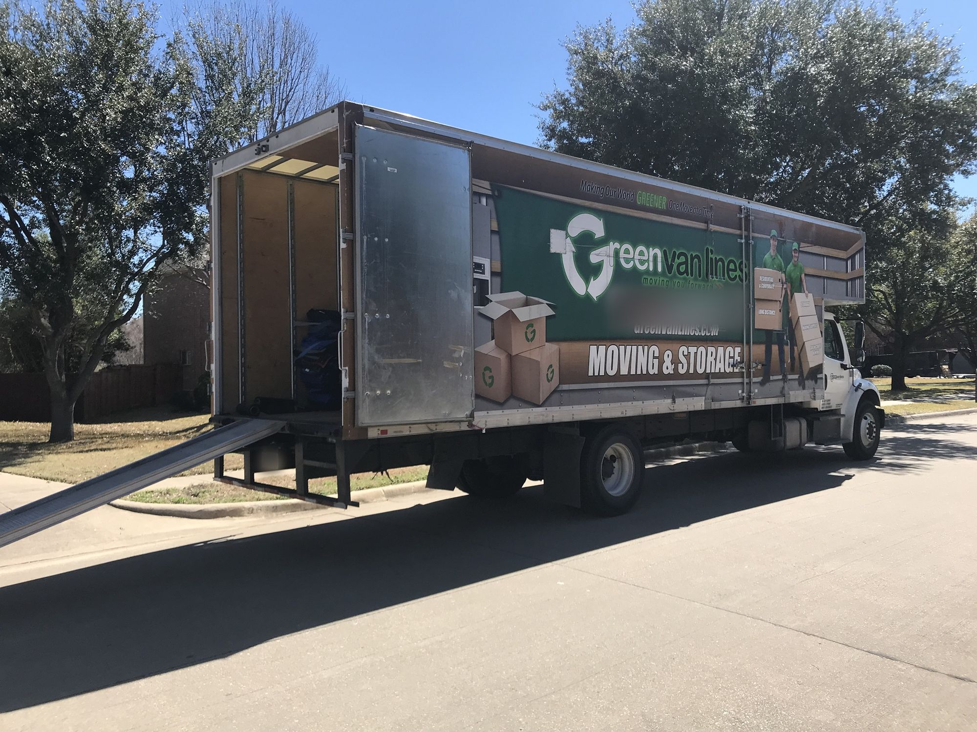 Green Van Lines moving truck parked on a tree-lined street with its loading ramp down